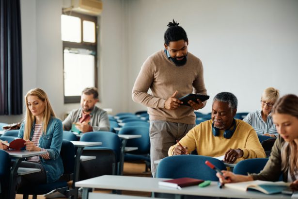Smiling black adult education teacher with his student in a lecture hall.